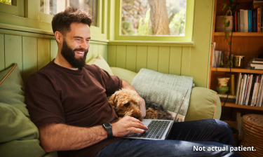 A man sitting with his dog while working on his laptop